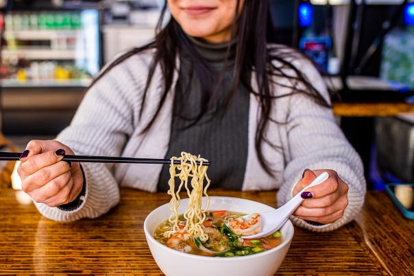 woman smiling while using chopsticks to eat a bowl of ramen