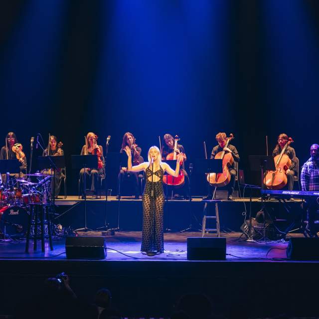 Grace Weber singing at a stand up mic with a string octet behind her