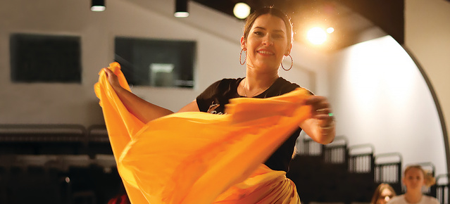 a traditional latino dancer in a goldenrod skirt smiling at the camera as she dances