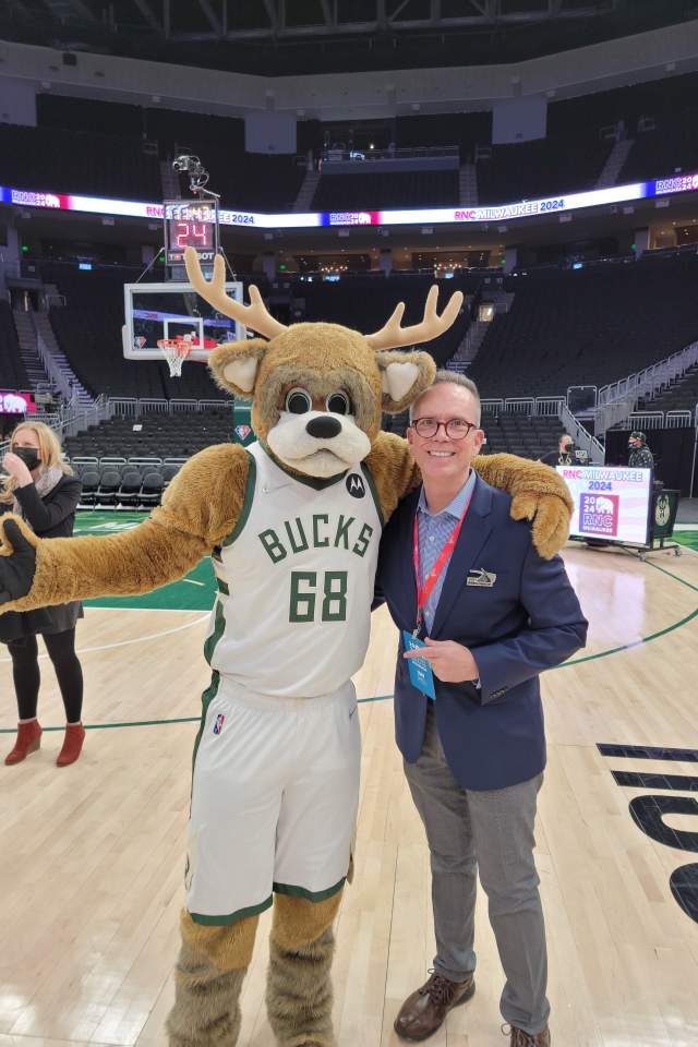 a man taking a photo with a mascot on the floor of a basketball arena