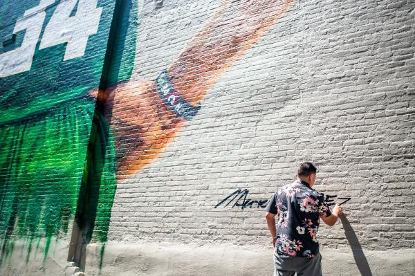 an artist using spray paint to sign a wall with a mural of a basketball player