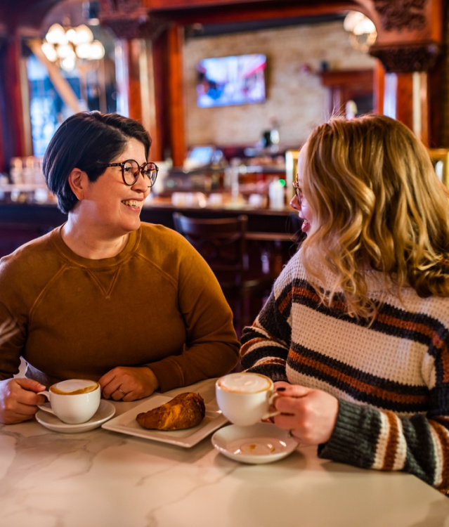 Two women smiling and drinking coffee in a cafe