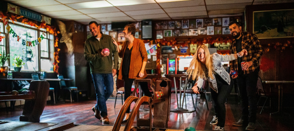 one person bowling in front of their friends in a dimly lit bowling alley