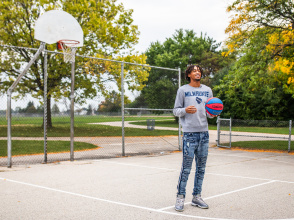 Learic Davis on an outdoor public basketball court, smiling and holding a basketball
