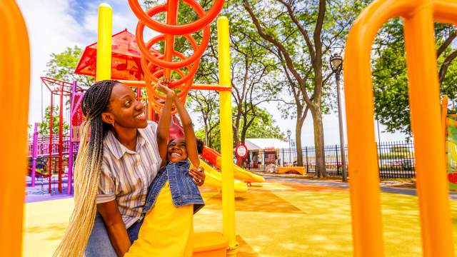 mom helping daughter swing on monkey bars