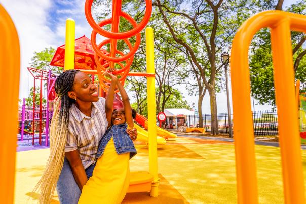 mom helping daughter swing on monkey bars