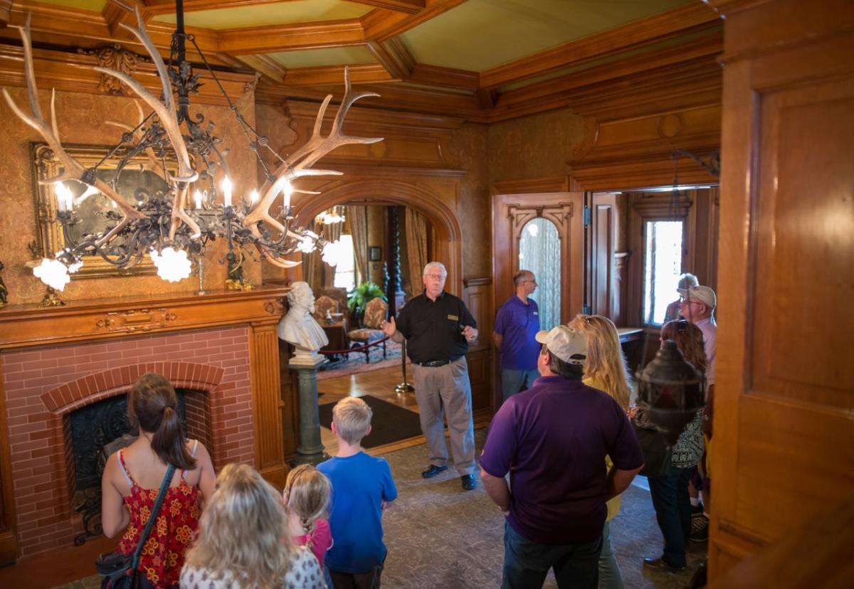 Pabst Mansion tour guide standing in the main hall presenting to a group gathered around him.