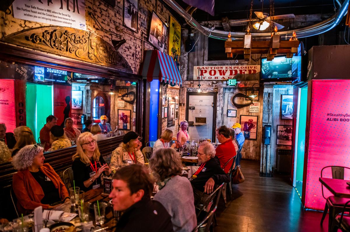 Interior of The SafeHouse, with a large group on the left and espionage-themed paraphernalia displayed throughout.