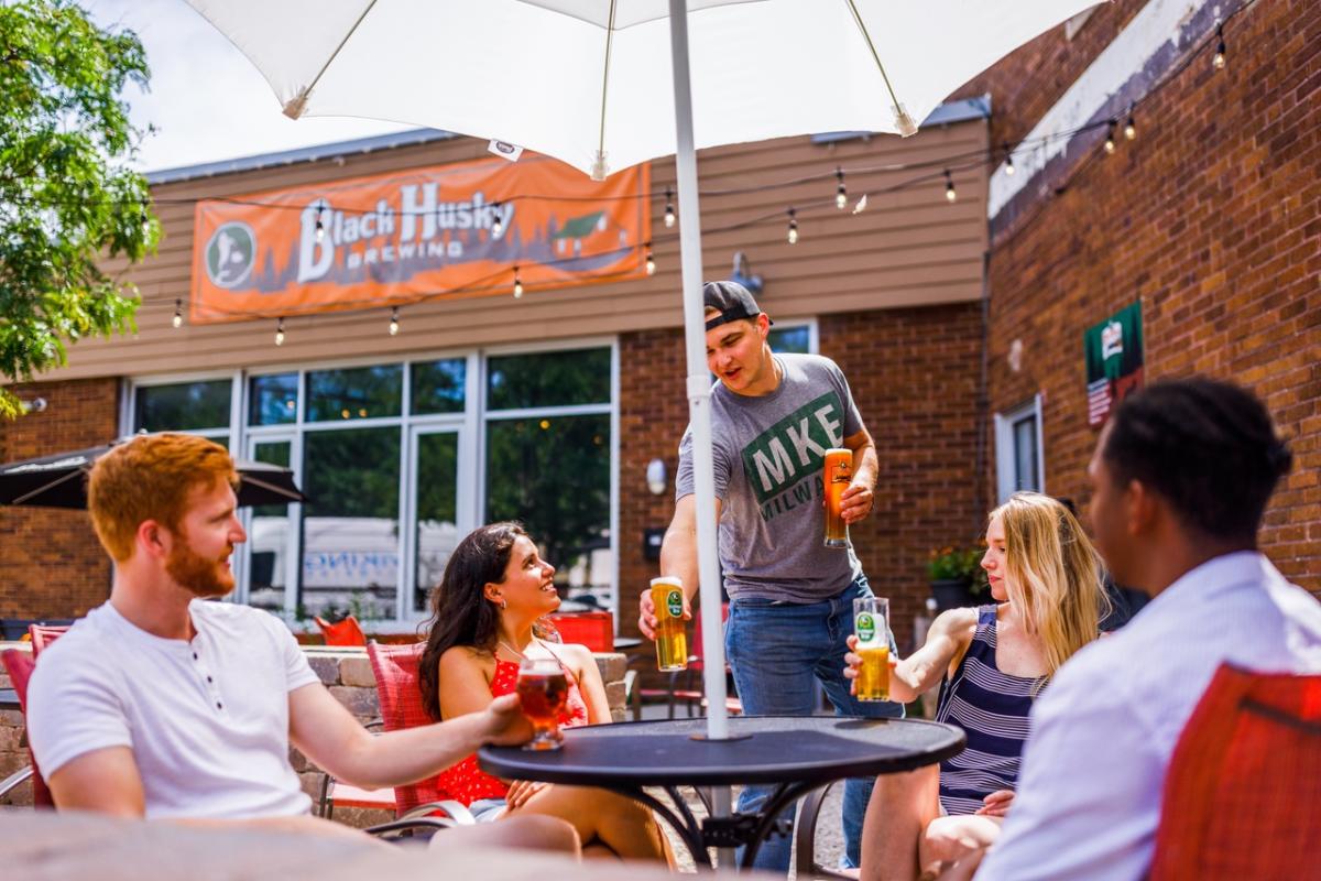 Group of friends sitting on the Black Husky patio, drinking beers