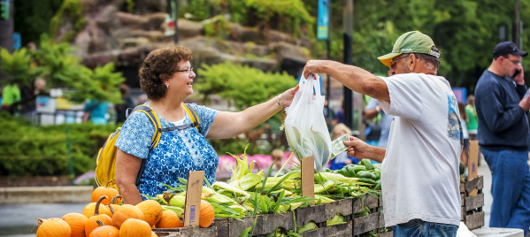 vegetable vendor handing buyer a bag of produce