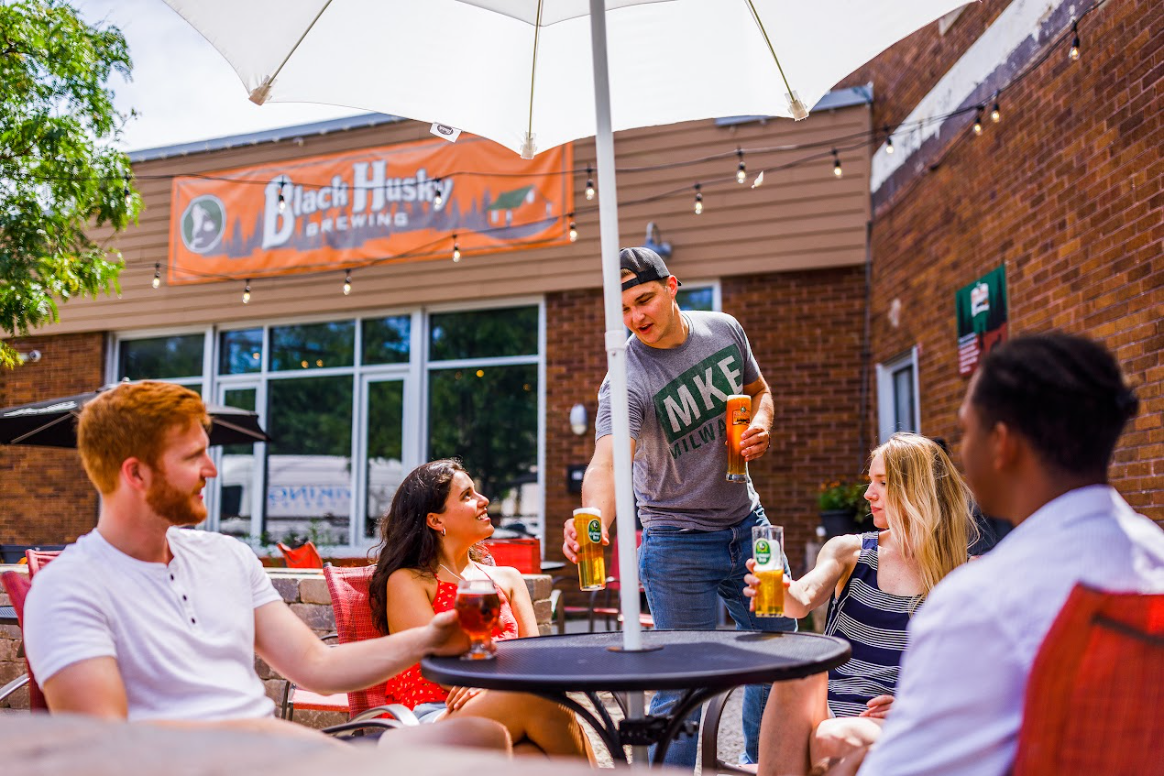 friends gathered around table outside of Black Husky Beer